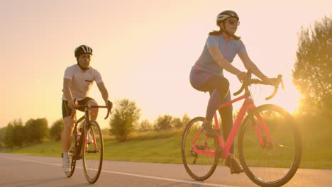 Two-professional-road-cyclists-ride-their-bikes-on-a-hill.-Hand-held-shot-of-two-strong-cyclists-female-and-male-on-their-training-on-a-warm-but-windy-summer-day